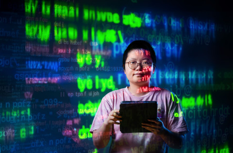 opiskelija selaamassa ipadia, taustalla juoksee koodi kirkkailla väreillä heijastettuna seinälle