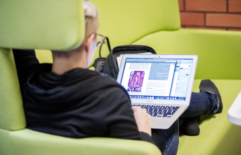 Nuori mies istuu sohvalla ja opiskelee etäyhteyden kautta.