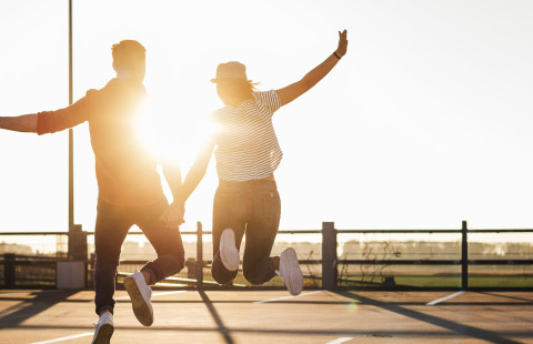 Photo of two people in the sun, holding hands and jumping from the ground.