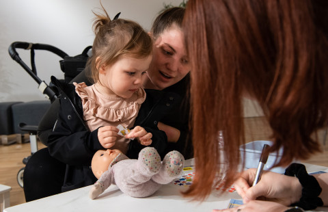 Nainen ja pieni lapsi käyttämässä pehmolelua nallesairaalassa.