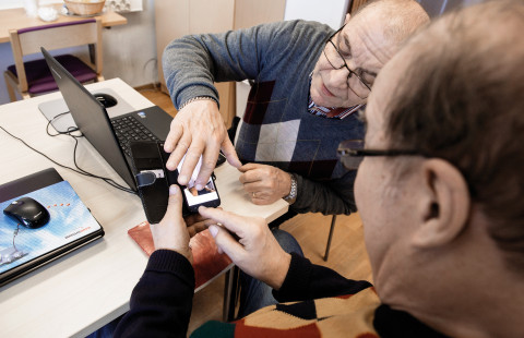 Photo of two older men using a laptop and a smart phone.