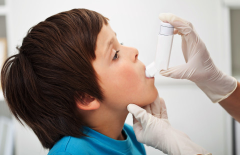 Aikuinen auttaa lasta käyttämään astmapiippua.