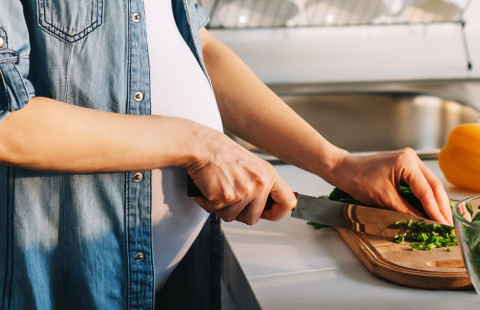 Raskaana oleva naineen laittaa ruokaa vihanneksista.