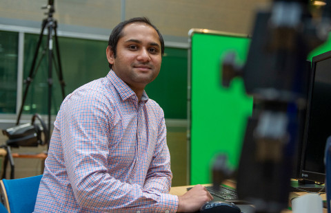 Man at his desk smiling and looking at the camera, computer on the desk.