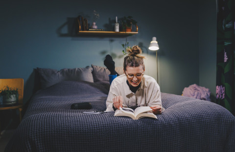 Nainen lukee kirjaa sängyllä maaten