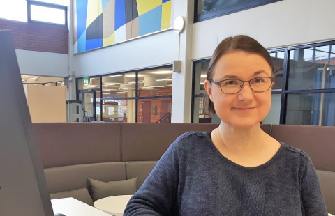 Kirjasto, nainen, tietokone, sohva.