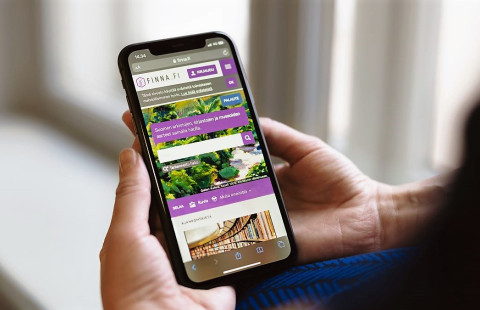 Ihminen pitelee molemmin käsin matkapuhelinta, jolla näkyy Finna.