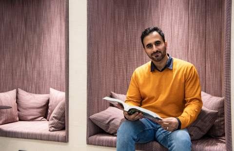 Dark haired with an orange shirt sitting and and holding a book