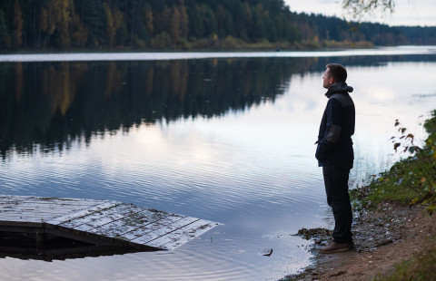 Yksinäinen mies seisoo järven rannalla.