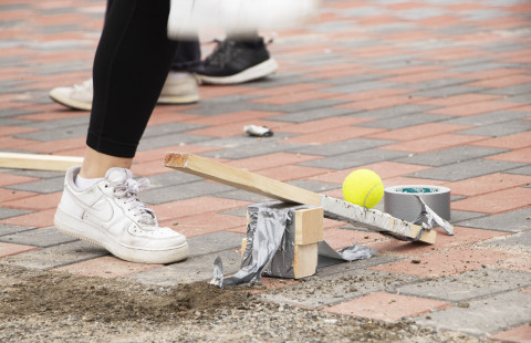 Lähikuvassa katapultti, joka sinkoaa keltaisen tennispallon kohti taivaita