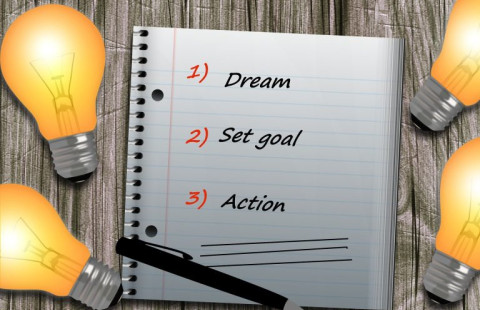 Muistilehtiö, hehkulamppuja. Lehtiössä teksti: 1) dream 2) set goal 3) action.