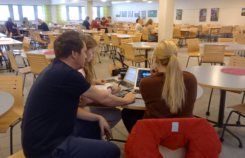 Opettaja opastaa kahta opiskelijaa pöydän ääressä