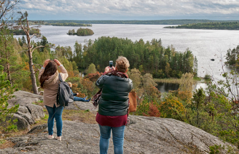 Kaksi naista ottaa korkealta mäeltä kuvia järvestä.