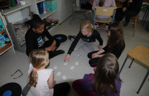 Teacher and pupils sitting on the floor playing cards.