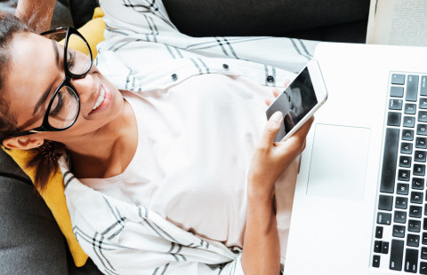 Woman working on a laptop and a cellular phone.