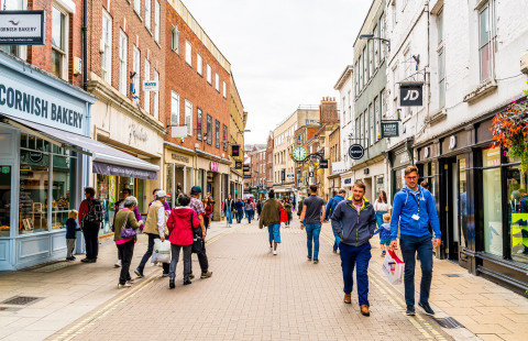 People walking along narrow street surrounded by houses.