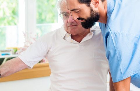 Hoitaja avustaa vanhaa miestä.