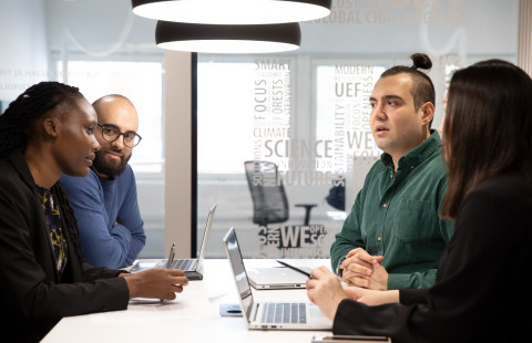 Neljä henkilöä neuvottelee pöydän äärellä aulatilassa.