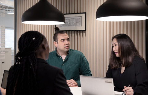 Kolme henkilöä neuvottelee pöydän äärellä aulatilassa.