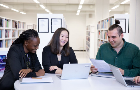 Kolme henkilöä keskustelee tiedokoneiden ja paperien äärellä.