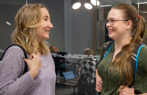 Kaksi opiskelijaa keskustelee iloisesti kampuksella.