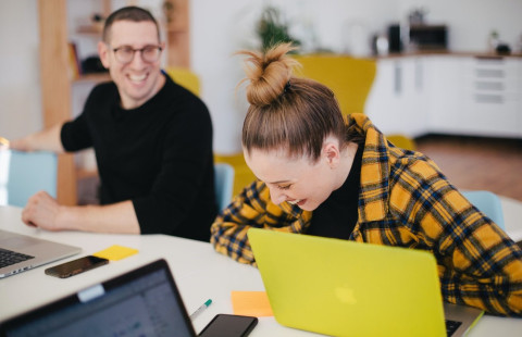 kaksi iloista ihmistä tietokoneiden ääressä.