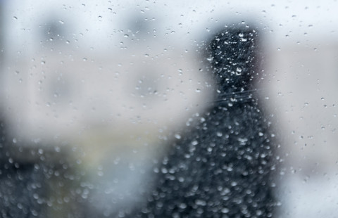 Hahmo sadepisaraisen ikkunan takana.