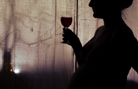 Raskaana oleva nainen viinilasi kädessään.