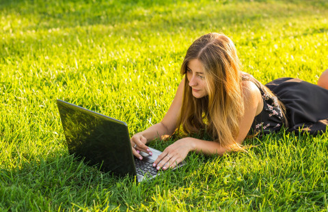 Nainen opiskelee nurmikolla tietokoneella. 