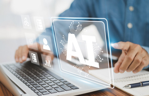 Käsi osoittaa tietokoneen käppäimistön päällä leijuvaa AI-tekstiä.