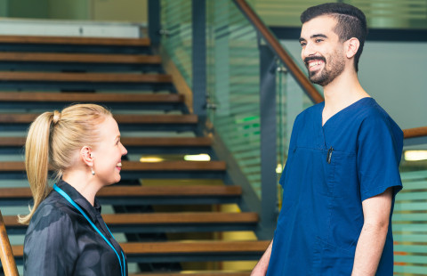 Kaksi hoitohenkilökuntaan kuuluvaa hymyilee toisilleen.