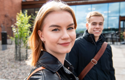 kaksi opiskelijaa Snellmania-rakennuksen ulkopuolella, kääntyneet katsomaan kameraan.
