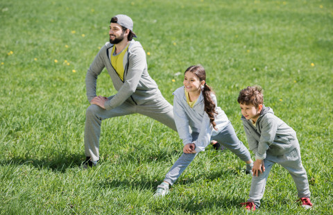 Isä ja lapset venyttelemässä ulkona.