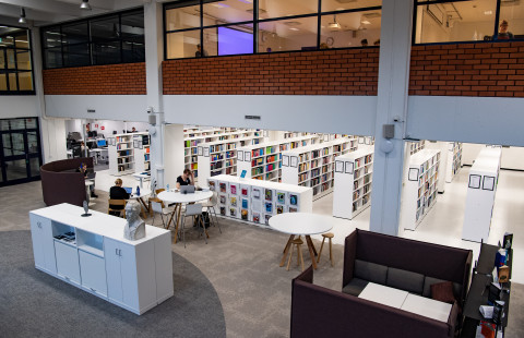 Yleiskuva Kuopion kampuskirjastosta. Kirjahyllyjä, lehtihyllyhä, lukupaikkoja, ihmisiä.