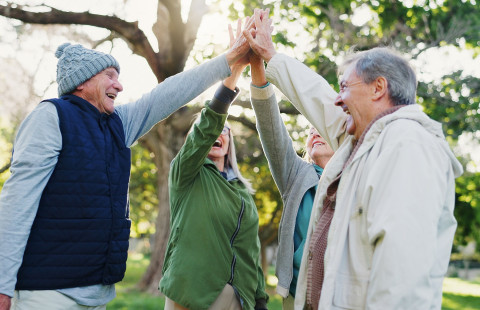 Neljä ikäihmistä liittää kädet yhteen päiden päällä.