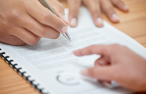 Kädet ja kynä dokumentin päällä.