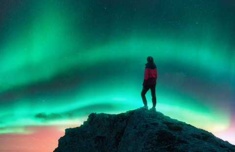 Henkilö katsomassa kukkulalla revontulia.