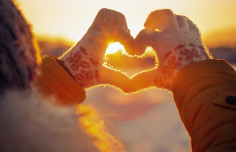 Kädet muodostavat sydämen auringonvaloa vasten talvella.