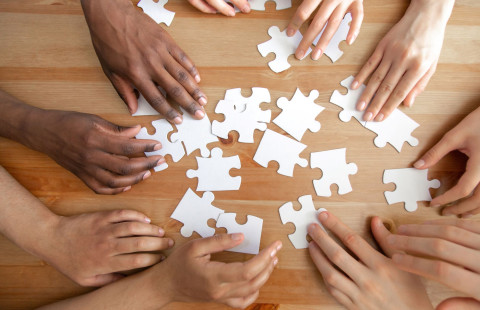 Palapelin paloja ja käsiä pöydän päällä.