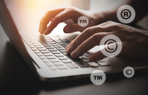 Sormet kannettavan tietokoneen näppäimistöllä immateriaalioikeussymbolien ympäröimänä.