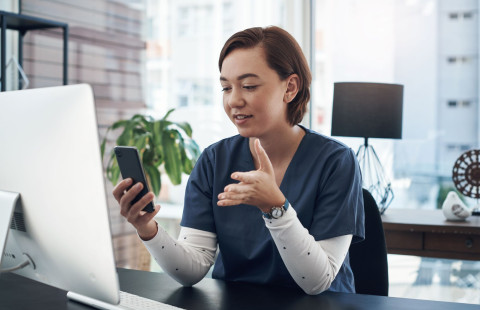 Sairaanhoitaja keskustelee mobiilipuhelin kädessään.