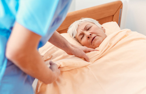 Hoitaja peittelee ikääntynyttä vuoteeseen.