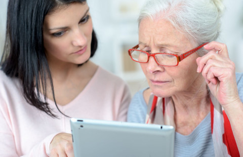 Nainen auttaa ikääntynyttä käyttämään tablettitietokonetta.