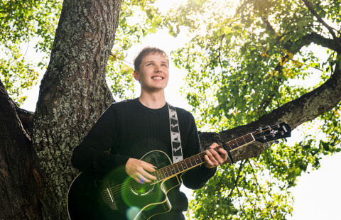 UEF-lähettiläs Konsta Kinnunen kitara kädessä puun alla