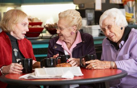 Kolme ikääntynyttä naista keskustelee kahvilan pöydän ääressä.