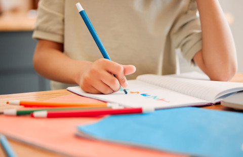 Nuori piirtää värikynien ympäröimään vihkoon.