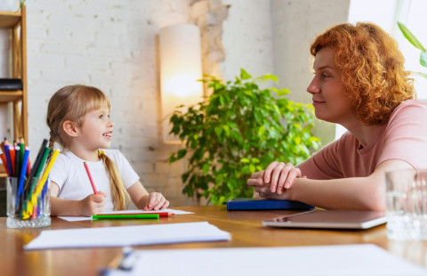 Aikuinen ammattilainen kommunikoi lapsen kanssa pöydän ääressä