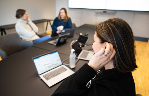 Meeting in a conference room, participant touching hearing aid.