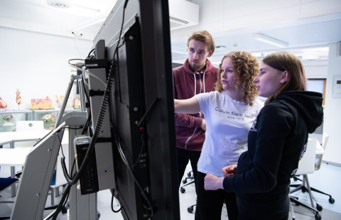 Kolme henkilöä katsoo tietoja isolta näytöltä