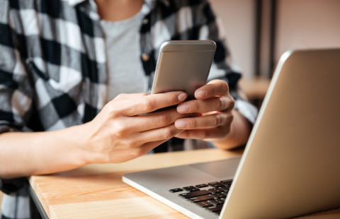 Henkilö selaa kännykkää kannettavan tietokoneen äärellä.